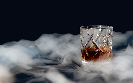 Стакан с янтарным алкоголем, окружённый дымом на тёмном фоне